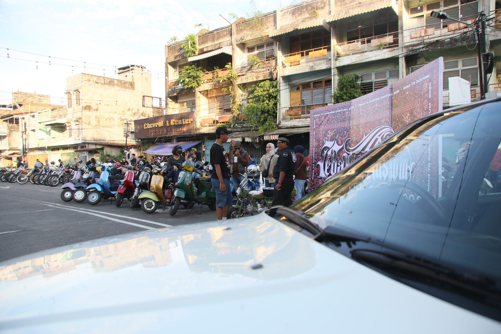 Deretan motor klasik dan skuter terparkir di kawasan Terminal Rawasari, dengan sekelompok orang berbincang di pinggir jalan berlatar bangunan tua.